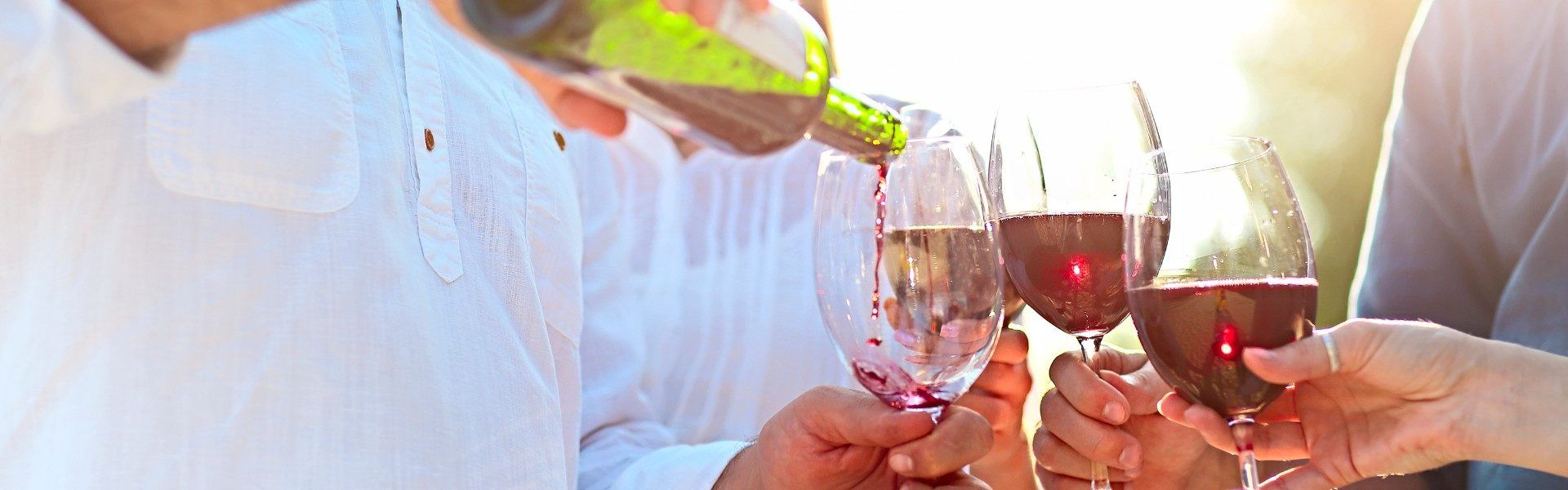 Three wine glasses with two full and pouring wine into the third