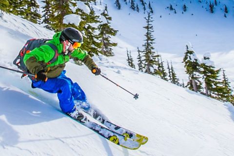 Downhill skiier skiing down mountain in blue pants and green jacket