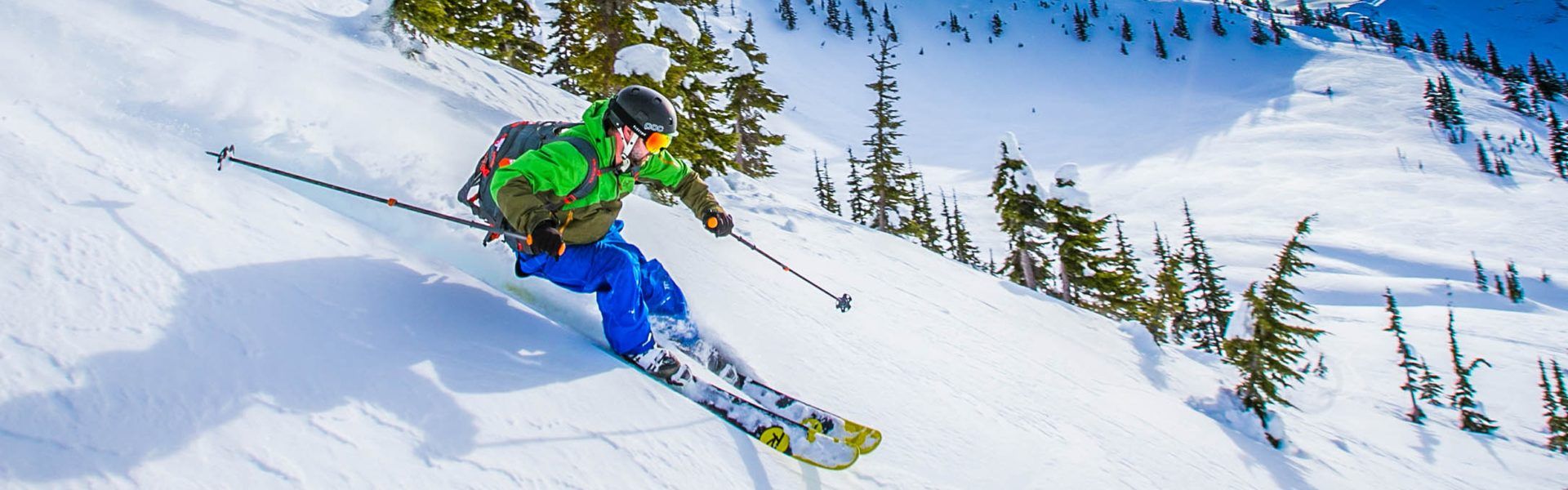 Downhill skiier skiing down mountain in blue pants and green jacket