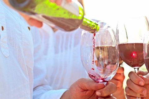 Three wine glasses with two full and pouring wine into the third